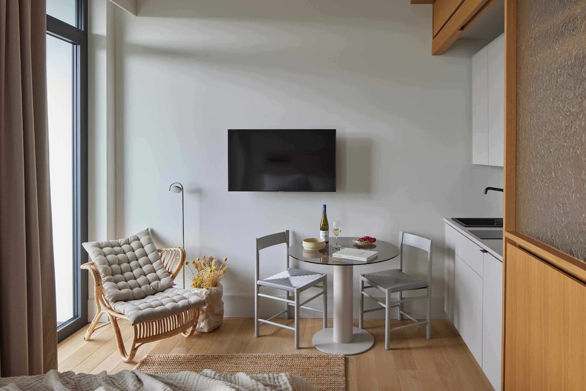 A modern room with a round dining table, two chairs, a sofa, a television, and a kitchen area.