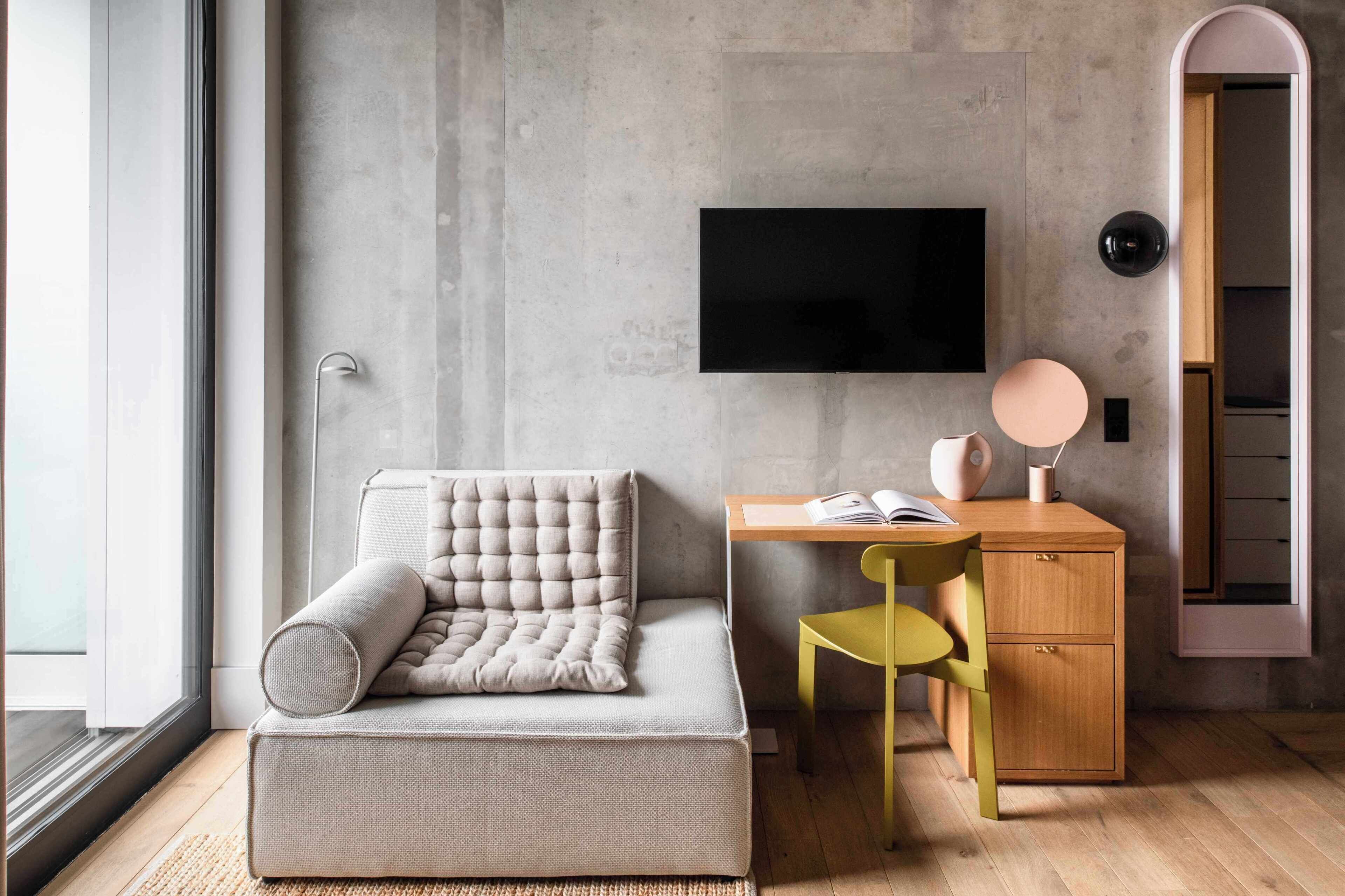 A modern room with a sofa, a desk, a chair, a television, and a door.