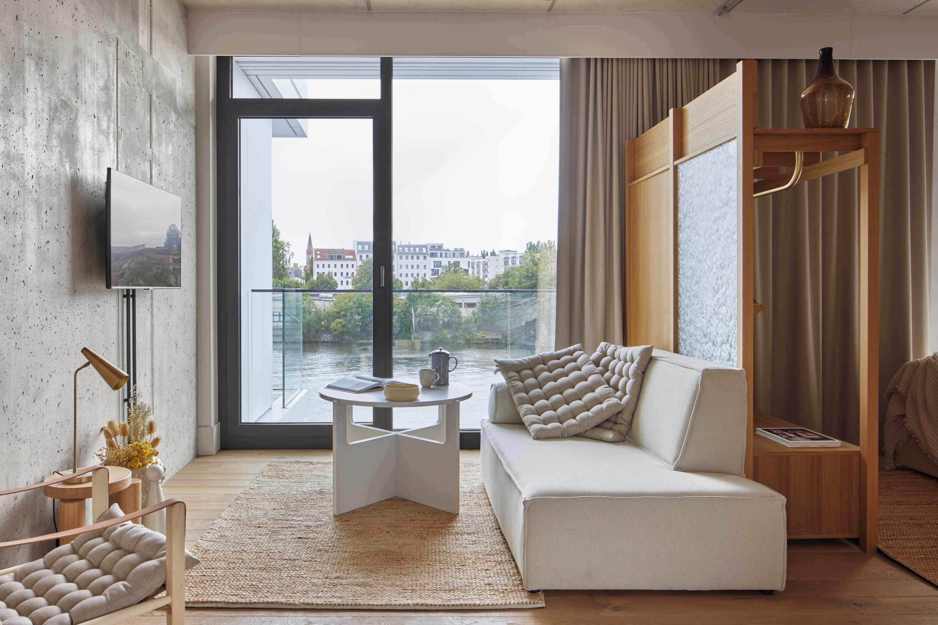 A modern living room with a sofa, a coffee table, a TV, and a large window with a view of buildings.