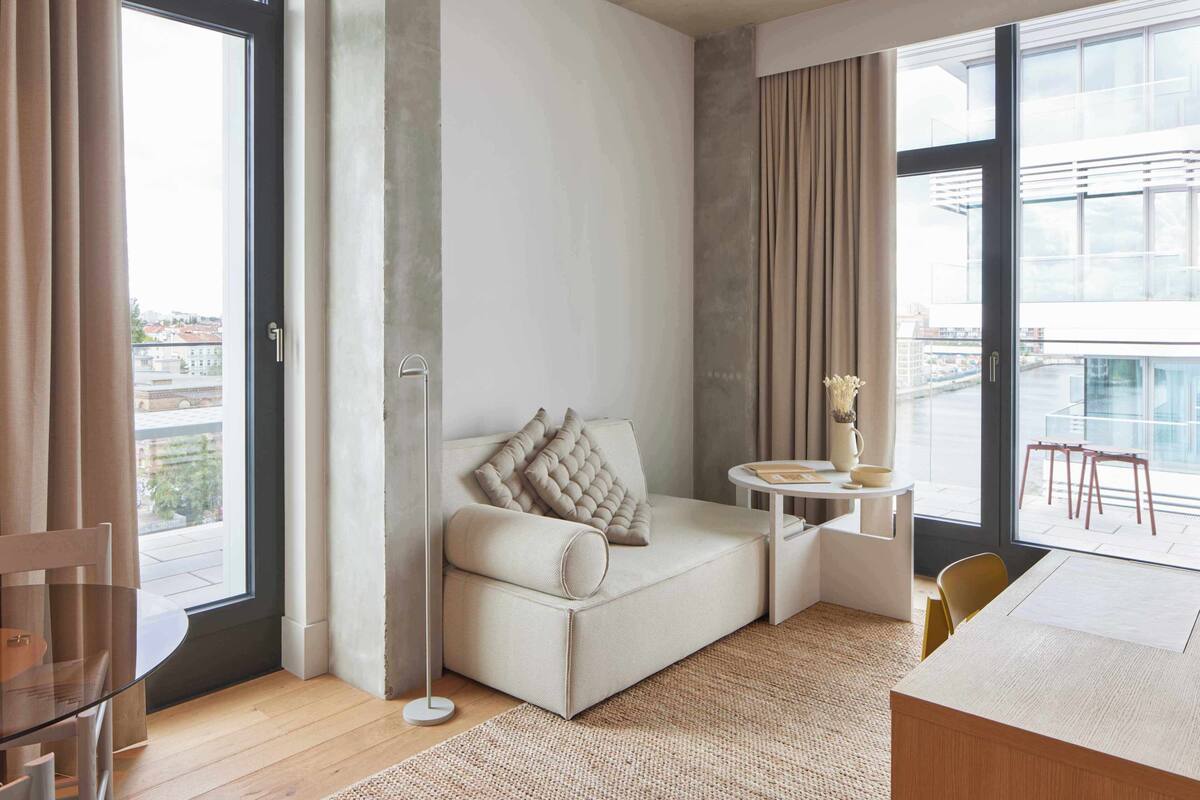 A modern living room with a sofa, a small table, and a view of the city through large windows.