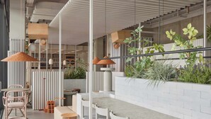 A modern interior with a long communal table, white chairs, and hanging pendant lights. - Locke at East Side Gallery (Berlin)