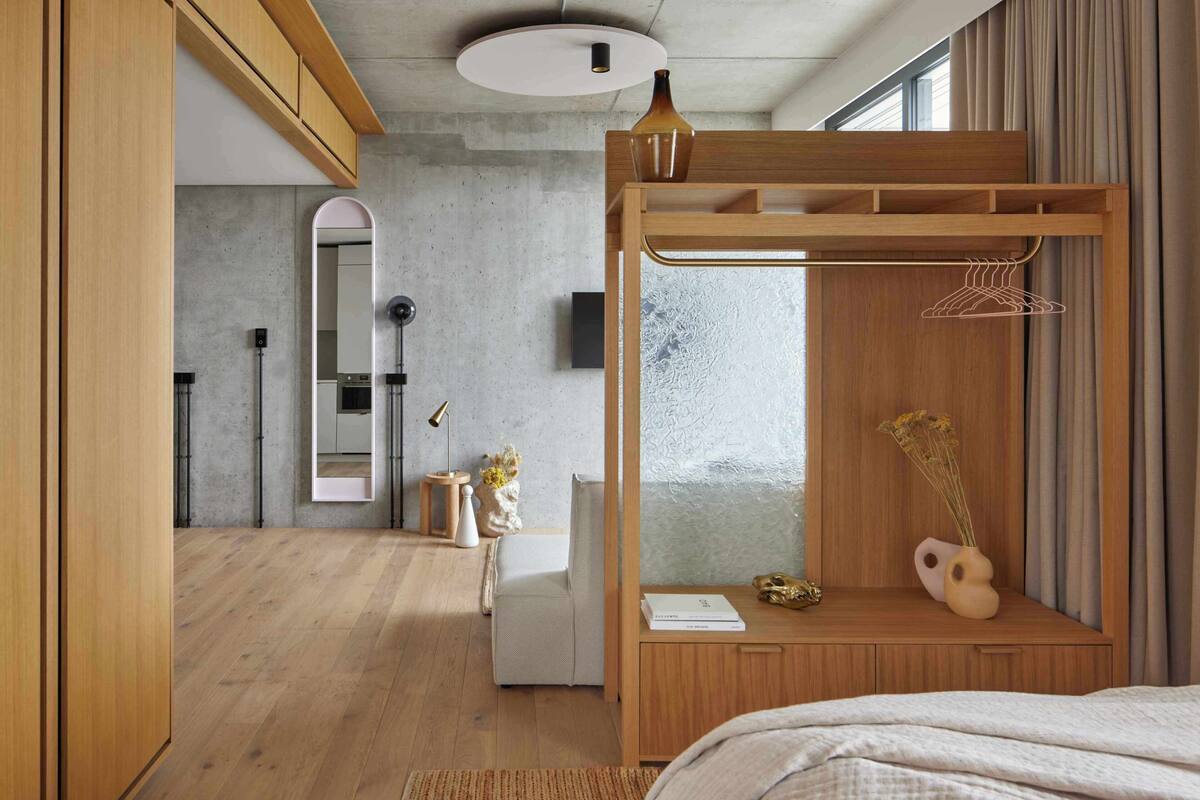 A modern bedroom with a wooden bed, a bedside table with a vase, and a wardrobe with a hanging rack.