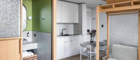 A modern room with a bed, a small kitchenette, a bathroom with a green wall, and a seating area with a table and chair.