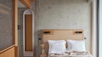 Una camera da letto con testiera in legno, un comodino con un libro e un vaso, e un'ampia finestra.
