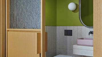 Ein Badezimmer mit einem Holzkosmetikschrank, einer weißen Toilette, einem pinken Waschbecken und einer grünen Wand.