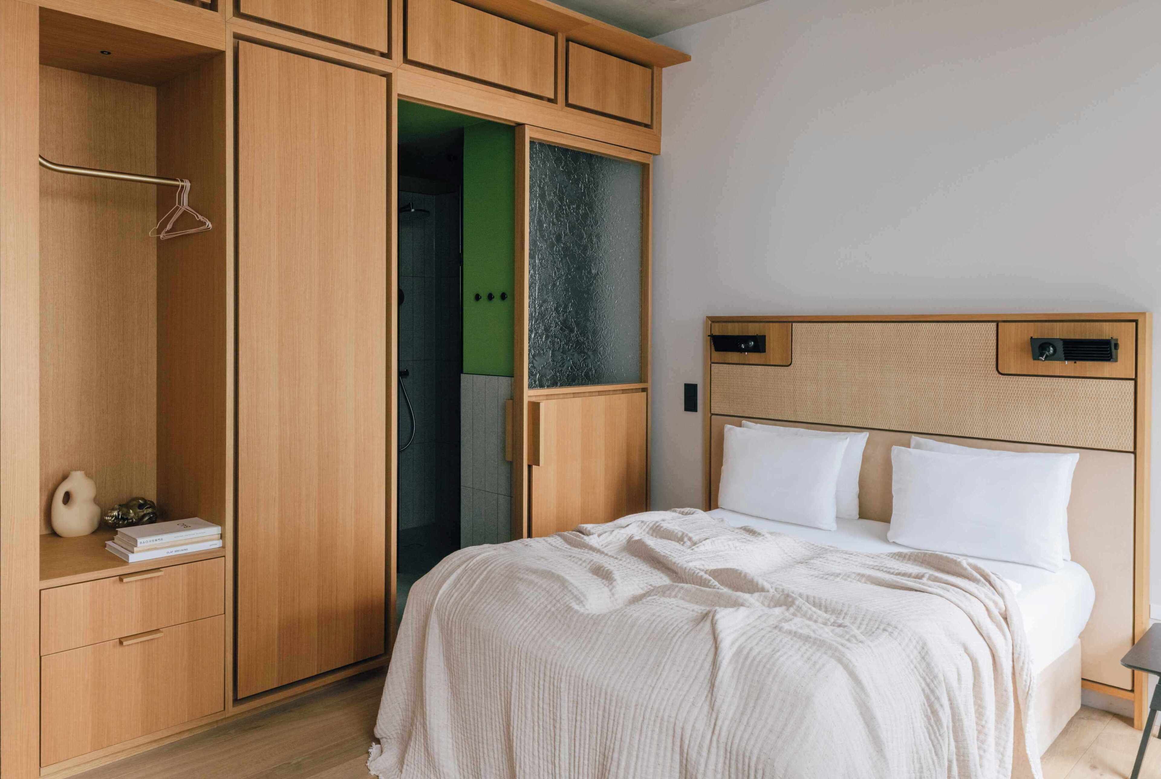 A bedroom with a bed, wooden wardrobe, and a bathroom visible through a glass door.