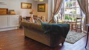 Un salón acogedor con sofá, mesa de comedor y zona de cocina con armarios y un radiador.