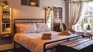 Un dormitorio con una cama con dosel, un armario de madera, un espejo, una ventana con cortinas y una lámpara.