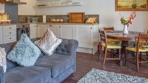 Una cocina moderna con armarios blancos, un sofá gris con cojines decorativos, una mesa de comedor con sillas y un cuadro en la pared.