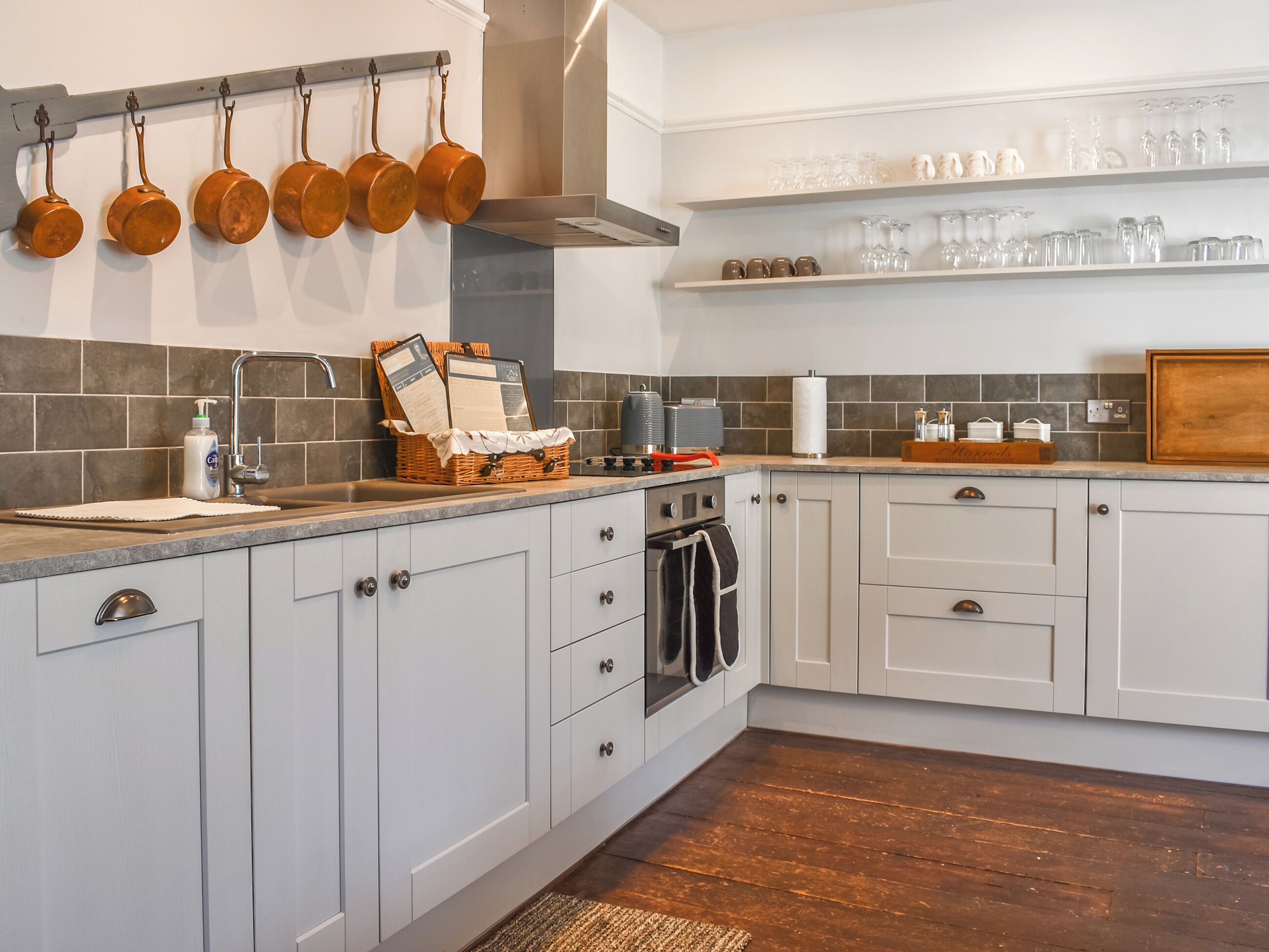 A kitchen with white cabinets, a wooden countertop, hanging pots, and shelves with glassware.