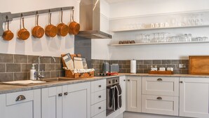 Una cocina con armarios blancos, encimera de madera, ollas colgantes y estantes con cristalería.