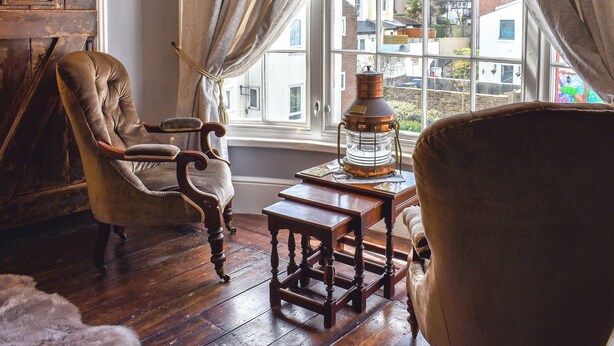 Una habitación con un ventanal grande, una silla de madera, una mesita y una lámpara antigua.