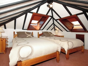 Ein Schlafzimmer mit zwei Holzbetten, einem Nachttisch mit Lampe und einem Fenster mit Blick zum Himmel.