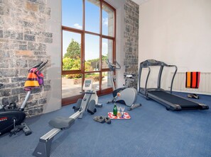 Ett gym med träningsutrustning, ett löpband och ett fönster med utsikt över grönområden.