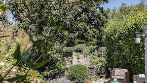 Um jardim com muro de pedra, móveis de exterior e diversas plantas e flores.