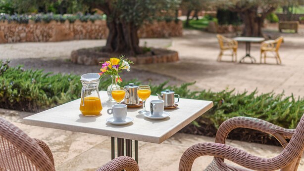 Uma área de refeições ao ar livre com mesa posta para o café da manhã, incluindo suco de laranja, xícaras de café e um jarro de suco de laranja.
