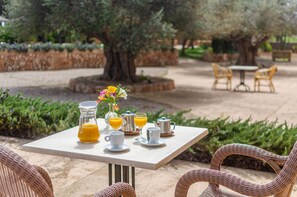 Un área de comedor al aire libre con una mesa lista para el desayuno, que incluye jugo de naranja, tazas de café y una jarra de jugo de naranja.