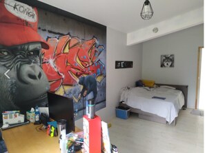 Um quarto com uma cama, uma escrivaninha com um computador e um mural grande na parede.