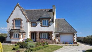 A two-story house with a garage, stone foundation, and a well-maintained garden.