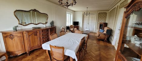 A dining room with a wooden herringbone floor, a large mirror, a chandelier, and a television in the background.