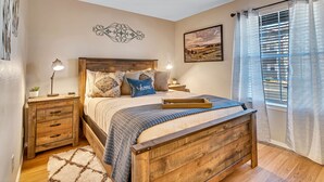 A bedroom with a wooden bed, bedside tables, a nightstand, a rug, and a window with curtains. - Freshly Remodeled Condo - Fall Creek Resort (Branson)