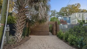 Een grindpad leidt naar een houten poort, omringd door diverse planten en een stroompaal.