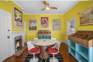 A dining room with a round table, four chairs, a fireplace, and various wall art.