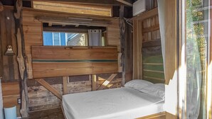Een houten hutje met een bed, een raam en een deur naar buiten.
