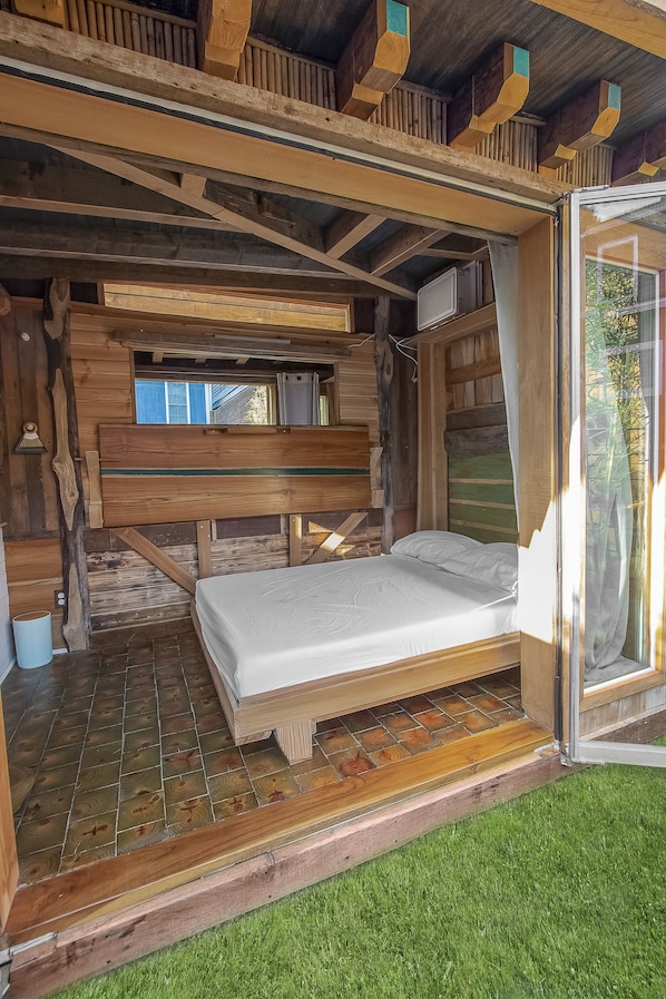 A wooden cabin with a bed, a window, and a door leading outside.