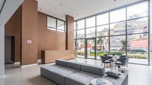 A modern lobby with a grey sectional sofa, a round coffee table, and a seating area with chairs. - Charlie Domy Paraíso (São Paulo)