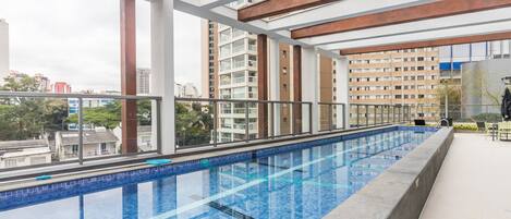 An indoor swimming pool with clear blue tiles, surrounded by a modern architectural design with large windows and a view of surrounding buildings.