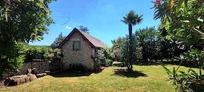 Um edifício de pedra com telhado inclinado, rodeado por um jardim relvado e várias árvores.