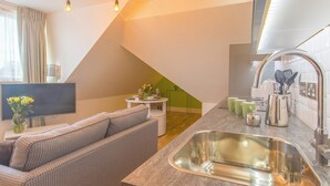 Een moderne keuken met een inbouwspoelbak, een zithoek met een bank en een televisie aan de muur.