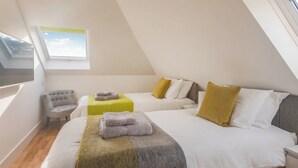 Een moderne, goed verlichte kamer met twee bedden, een fauteuil en een raam dat voor natuurlijk licht zorgt.