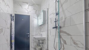 Een badkamer met een donkere deur, een douchecabine van glas en een wastafel met een marmeren spatwand.