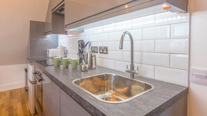 Een moderne keuken met een RVS-spoelbak, een witte betegelde achterwand en een grijs aanrecht.