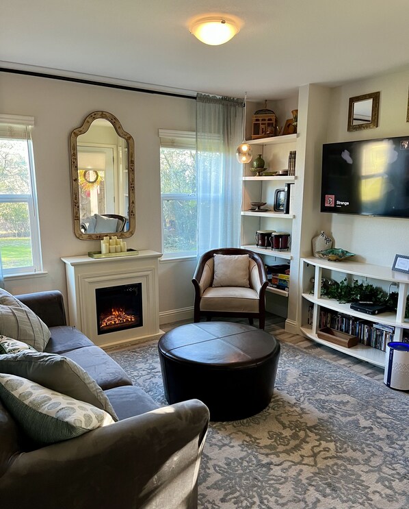 A cozy living room with a fireplace, comfortable seating, a television, and a bookshelf.