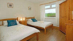 A bedroom with two wooden beds, bedside lamps, a wardrobe, and a window with a view of the countryside. - 4 bedroom accommodation in Llanhrian, nr Haverfordwest (Llanhrian, nr Haverfordwest)