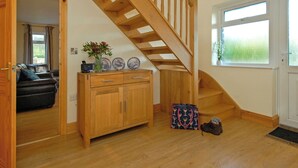 A wooden staircase, a sofa, a cabinet, a vase with flowers, and a window with a view. - 4 bedroom accommodation in Llanhrian, nr Haverfordwest (Llanhrian, nr Haverfordwest)
