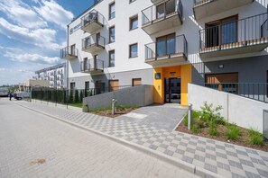 A multi-story residential building with balconies, a gated entrance, and a paved walkway.