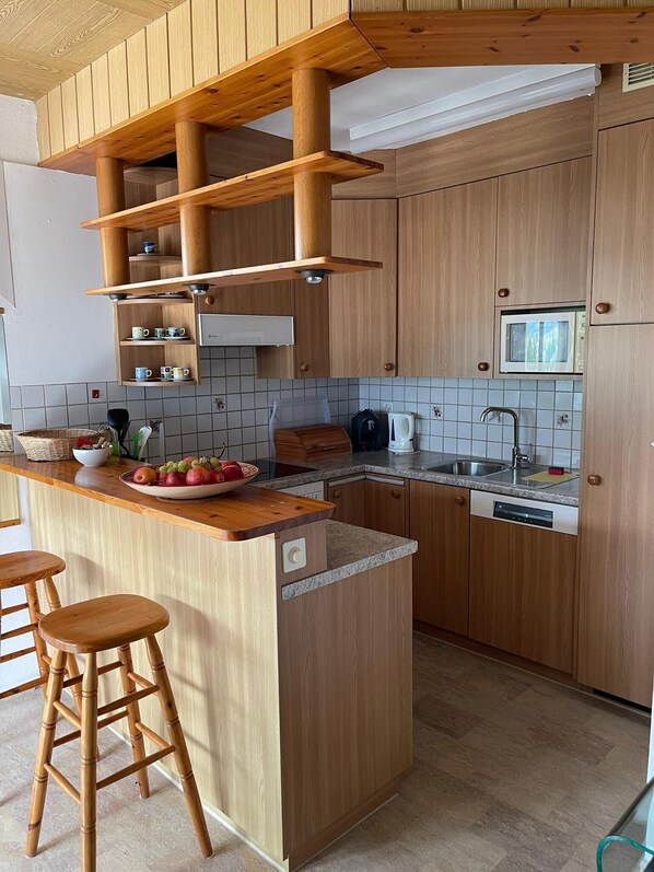 A modern kitchen with wooden cabinetry, a central island with stools, a microwave, and a dishwasher.