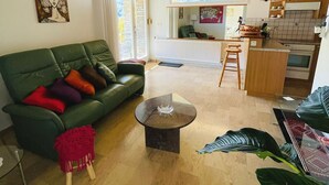 A living room with a green sofa, a small coffee table, and a view of a kitchen and dining area through an open door.