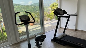 A home gym with an elliptical and a treadmill, large windows with a view of a green landscape.