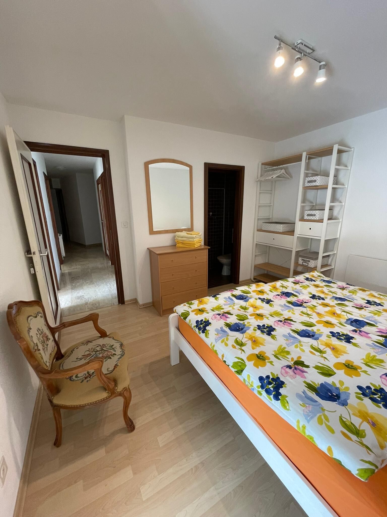 Un dormitorio con una cama, un aparador de madera, un espejo, un armario y una silla.