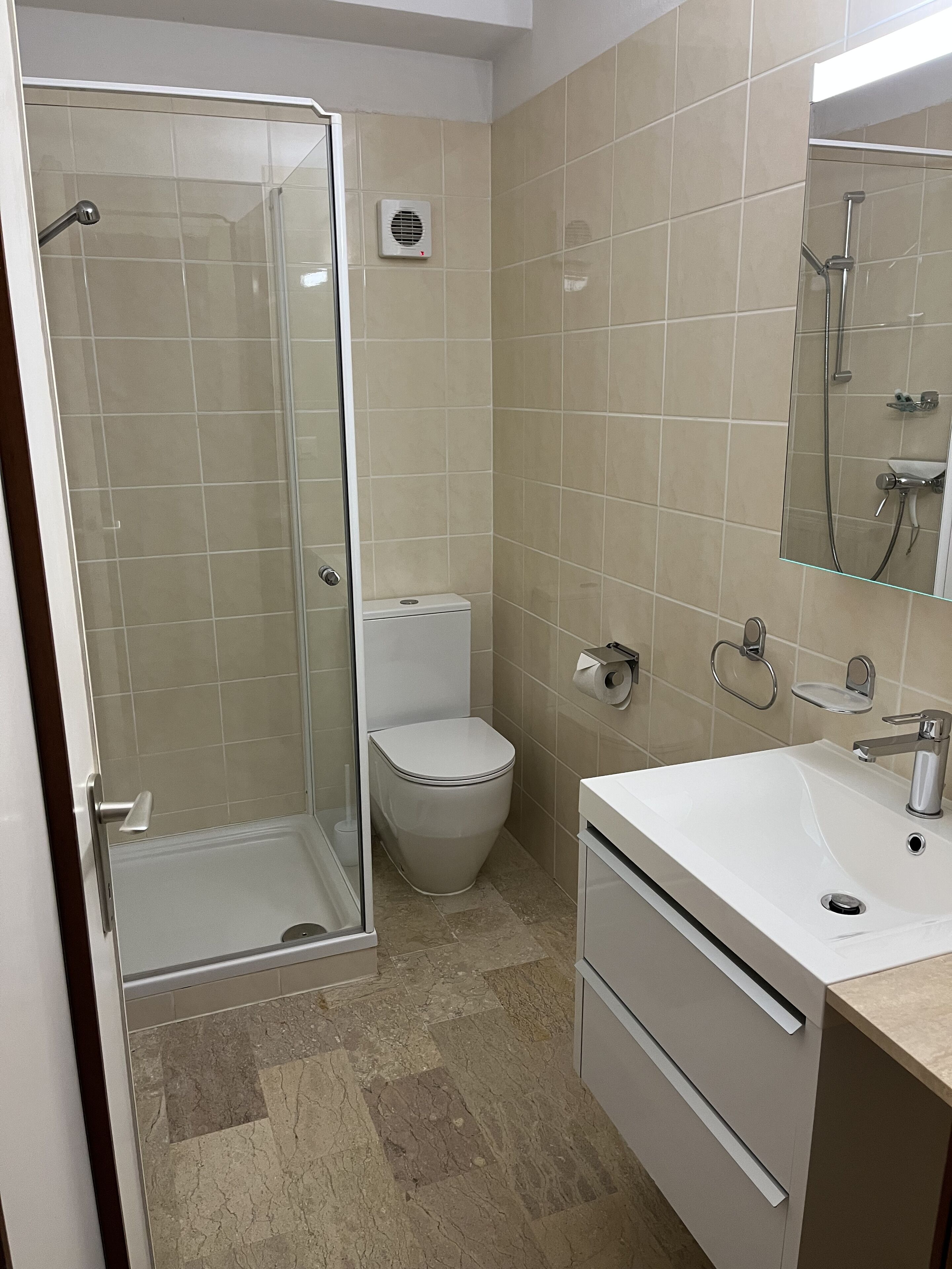 Un baño moderno con cabina de ducha de vidrio, inodoro, lavabo y espejo.