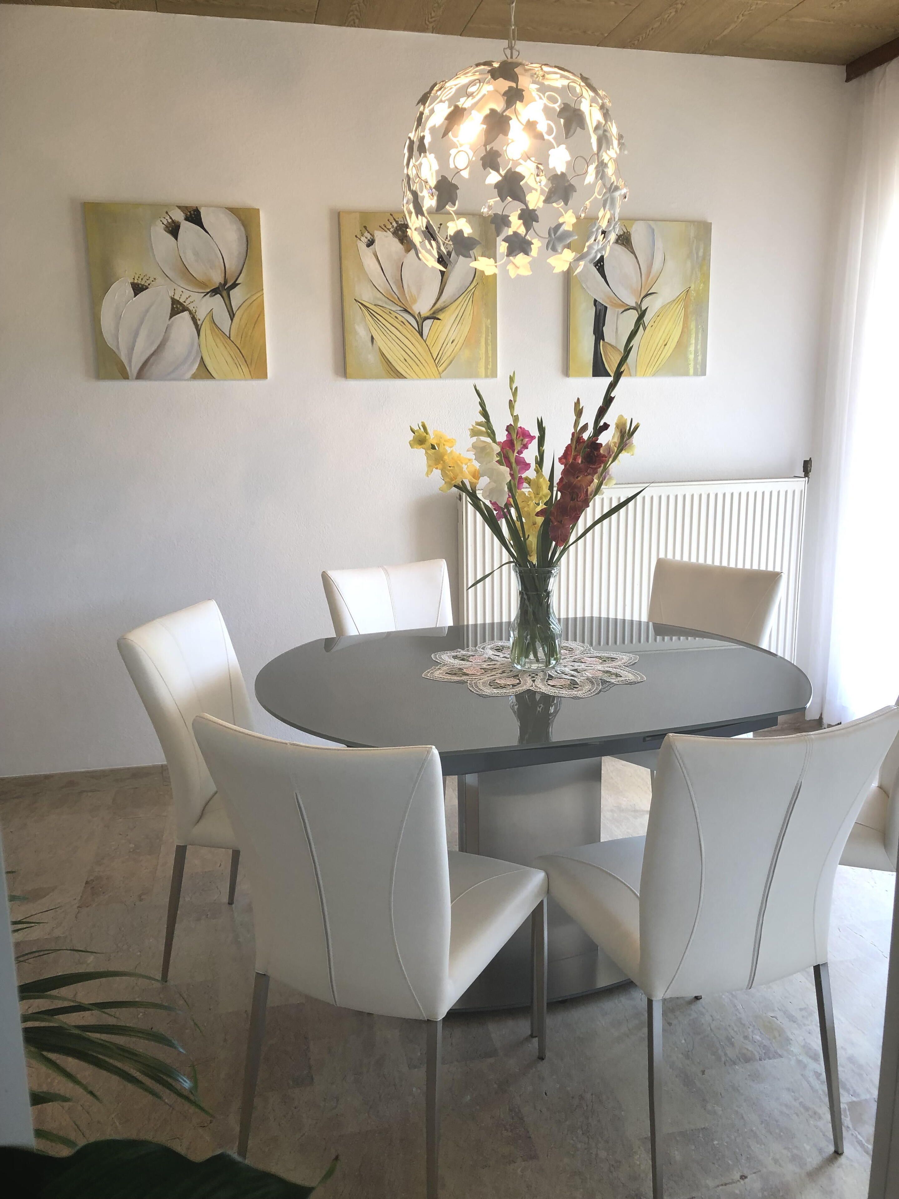 Un coin repas avec une table ronde, des chaises blanches, un vase de fleurs et des œuvres d’art murales.