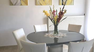 Un coin repas avec une table ronde, des chaises blanches, un vase de fleurs et des œuvres d’art murales.