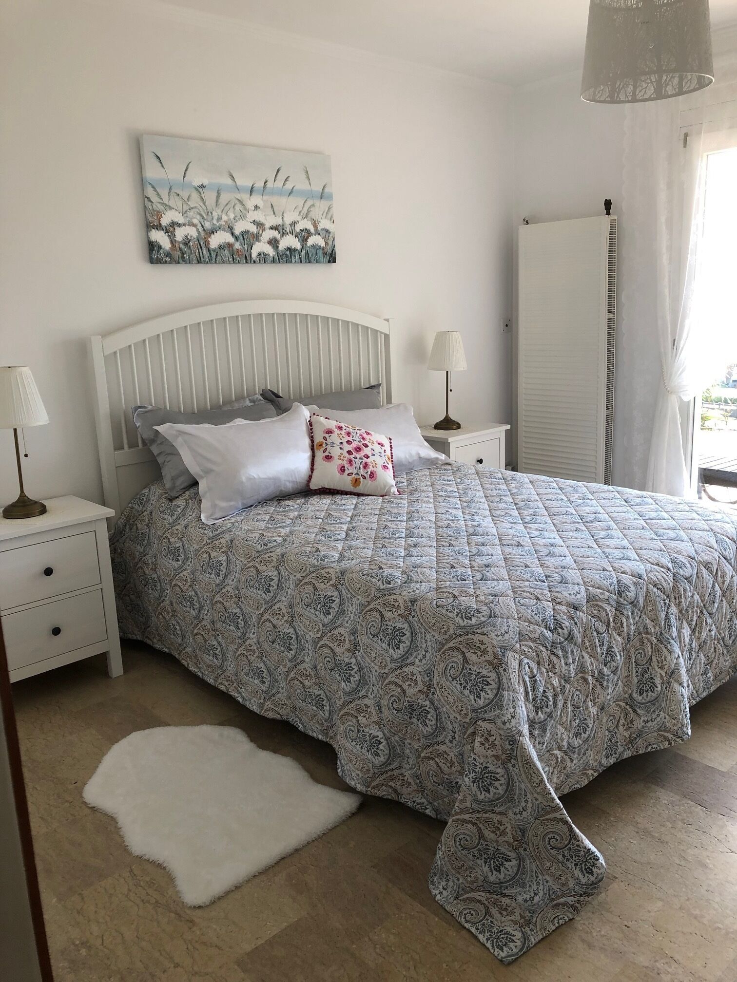 Een slaapkamer met een bed, nachtkastjes, een lamp, een wit tapijt en een schilderij aan de muur.