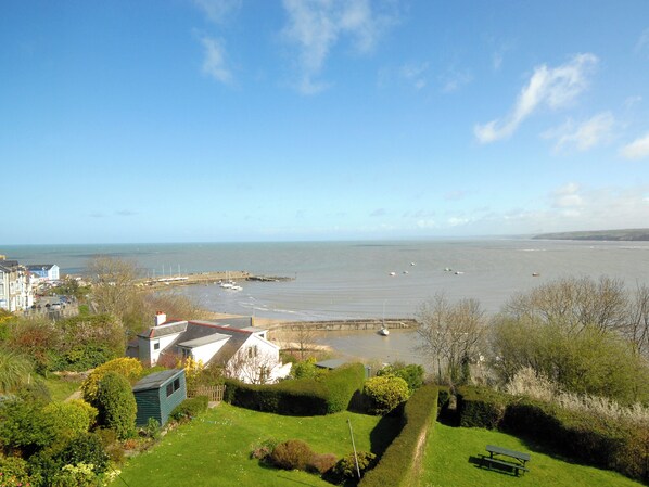 A coastal view with a grassy area, a bench, and a small house. - 4 bedroom accommodation in New Quay, near Cardigan (New Quay, near Cardigan)