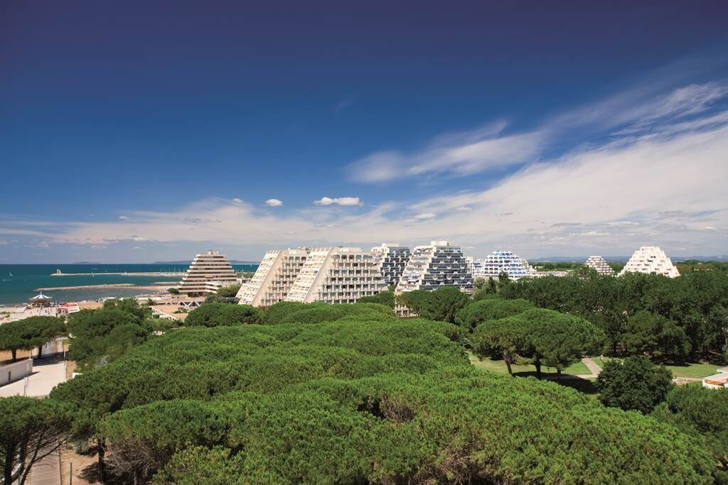 A coastal resort with pyramid-shaped buildings, lush greenery, and a view of the sea.